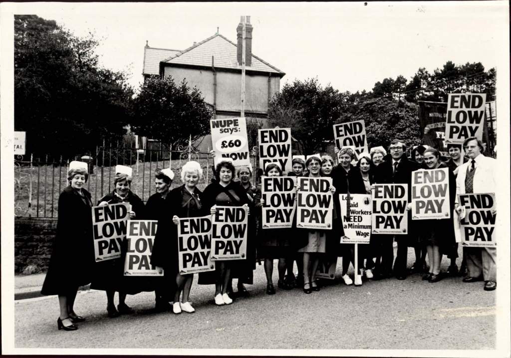 Picture of public service workers holding protest signs that read 'end low pay'.