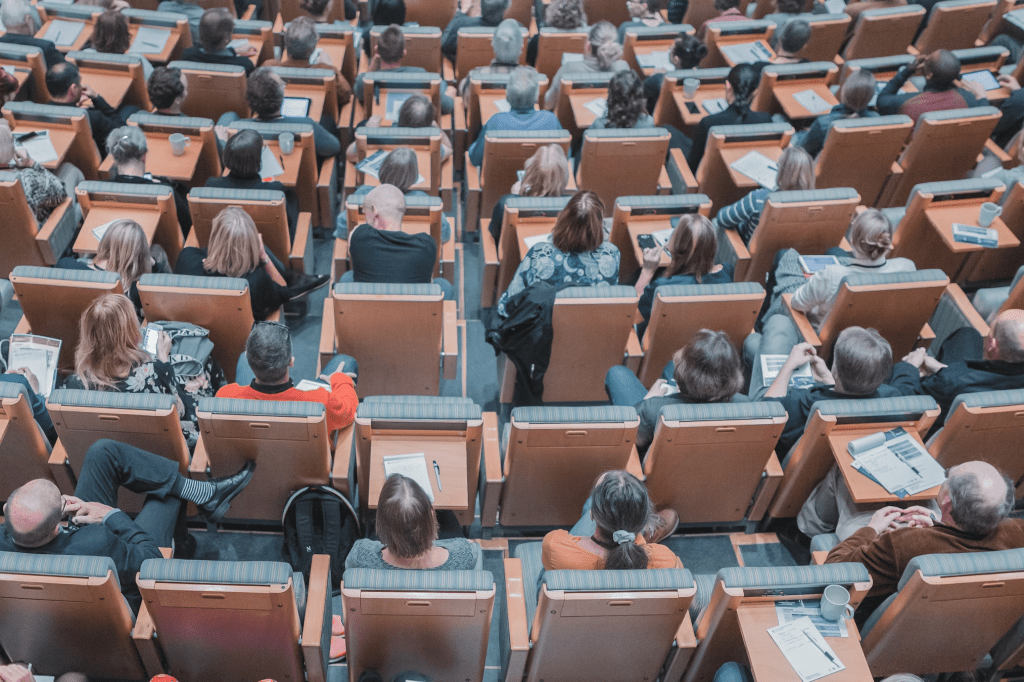 Aerial view of a lecture theatre, looking downwards at the people sat in the chairs below.