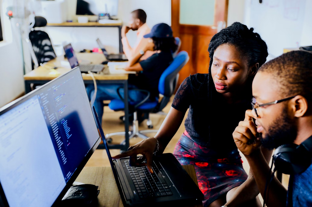 Woman and man sat at a table looking at a computer monitor together.