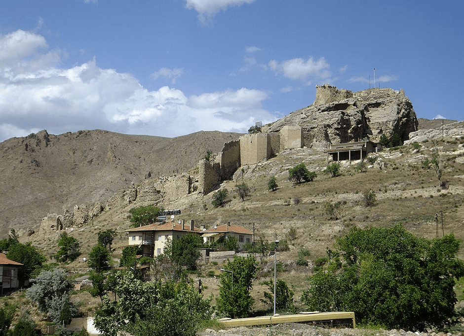 A photograph of ruins of an ancient fortress, in modern day Divriği, that sits on the side of a hill under a blue sky.