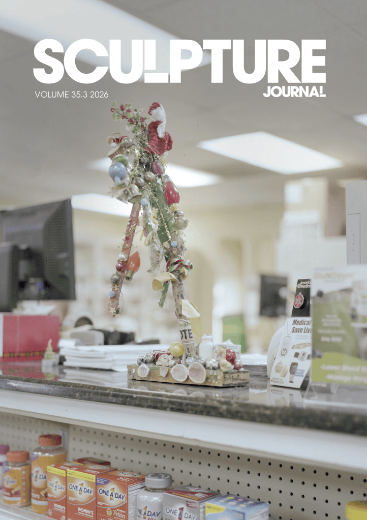 Cover of Sculpture Journal Volume 35.3 (2026), featuring a small mixed-media sculpture displayed on a pharmacy counter. The assemblage is decorated with artificial flowers, ribbons, ornaments and festive light bulbs, and stands on a rectangular base surrounded by shells and decorative objects. Shelves of vitamin products and a softly blurred retail interior appear in the background. The journal title “SCULPTURE JOURNAL” is displayed prominently across the top.